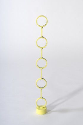 Abstrakcyjna rzeźba z niedokładnie pomalowanej na żółto stali. Tworzy ją kilka okręgów ustawionych jeden na drugim w rodzaj kolumny lub totemu. Pięć pierścieni i cztery pełne koła takiej samej wielkości ułożone są naprzemienie. Wszystkie pierścienie zwróco