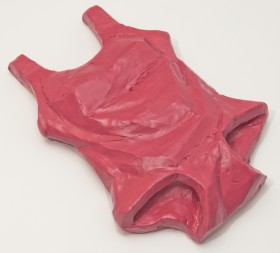 Rzeźba wykonana z plasteliny. Realistycznie przedstawiony jednoczęściowy damski kostium kąpielowy w kolorze różowym. Kostium położony płasko na podłożu. Zaznaczone fałdki materiału i lekkie wybrzuszenia w miejscu piersi.